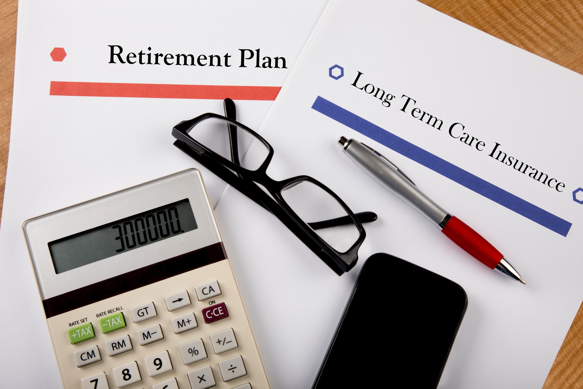 Retirement Plan, Long Term Health Insurance documents with calculator, cell phone, and glasses